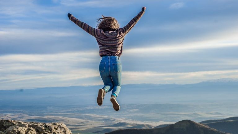 Person jumping on a mountain peak, celebrating adventure and freedom.